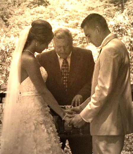 A bride and groom holding hands while the officiant holds something.