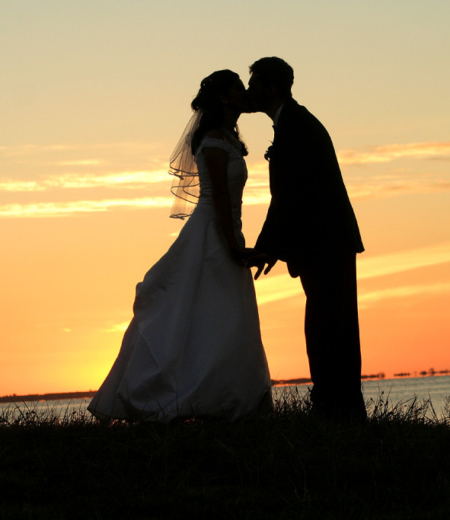 A bride and groom kissing in front of the sunset.